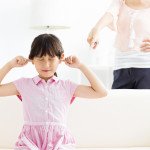 Upset little girl covering her ears while her mother angry